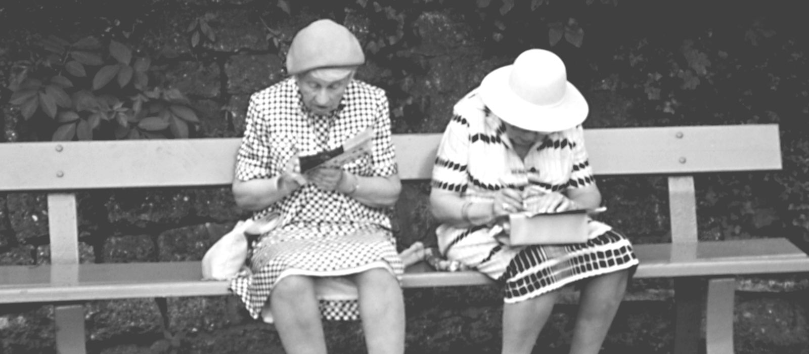Zwei Frauen mit Hut sitzen lesend auf einer Parkbank, 1960